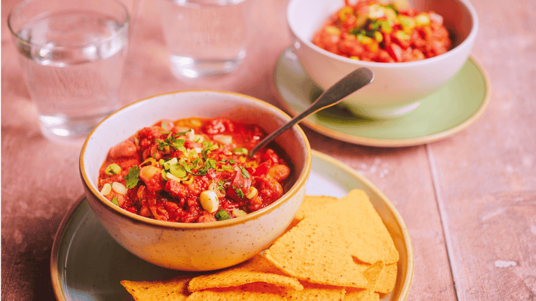 Bowl of mixed bean chilli topped with spring onions and fresh herbs, served with tortilla chips on a place in the Giant's Causeway Visitor Centre Café